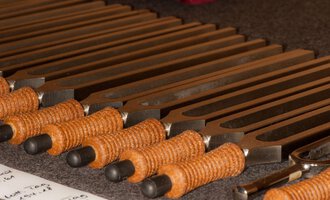 A series of tuning forks with orange handles is lying on a tabletop. In the background, some notes are visible. | © Bio-Hotel Oswalda Hus | Joachim Weiler
