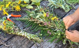 A table with fresh herbs and colorful flowers. Someone is tying a herb wreath with scissors beside it. | © Kleinwalsertal Tourismus | Lydia Fritz-Ilg