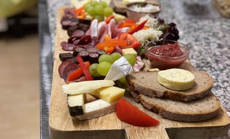 Ein reichhaltiges Käse- und Wurstbrett mit frischem Brot, Trauben, Paprika und verschiedenen Dips. Ideal für einen geselligen Snack oder eine Party. | © Kuhstall | Uwe Nagel