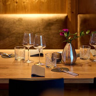 Ein schön gedeckter Tisch in einem gemütlichen Restaurant. Er ist mit Gläsern, Besteck und einer Vase mit Blumen dekoriert. | © La Vallée | Annette Sandner