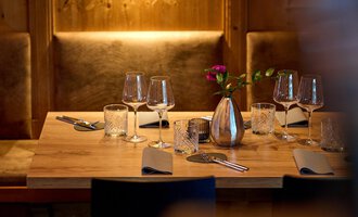 Ein schön gedeckter Tisch in einem gemütlichen Restaurant. Er ist mit Gläsern, Besteck und einer Vase mit Blumen dekoriert. | © La Vallée | Annette Sandner