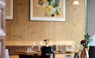 Ein gemütliches Restaurant mit Holzdekor und stilvollen Tischen. Auf einem Tisch stehen Gläser und eine kleine Blumenvase. | © La Vallée | Annette Sandner