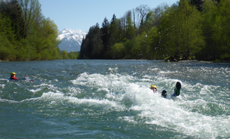 Ein Fluss mit schäumendem Wasser und grünen Bäumen am Ufer. Im Hintergrund sind schneebedeckte Berge zu sehen. | © MAP-Erlebnis