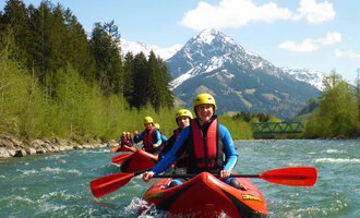 Eine Gruppe von Kajakfahrern paddelt auf einem klaren Fluss. Im Hintergrund sind schneebedeckte Berge und grüne Bäume zu sehen. | © MAP-Erlebnis