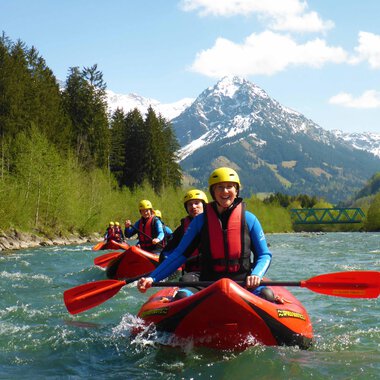 Eine Gruppe von Kajakfahrern paddelt auf einem klaren Fluss. Im Hintergrund sind schneebedeckte Berge und grüne Bäume zu sehen. | © MAP-Erlebnis