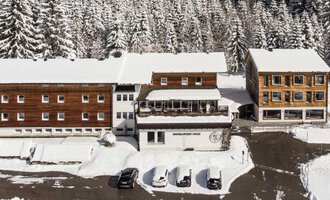 Eine schneebedeckte Landschaft mit mehreren Gebäuden im Chalet-Stil. Umgeben von hohen, schneebedeckten Tannenbäumen. | © Marburger Haus | Sweetchili