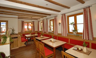 A cozy restaurant with wooden ceilings and red benches. The windows let in a lot of light and there are some plants as decoration. | © Michl das Steakhaus | Johannes Littich