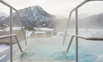 Ein moderner Wellnessbereich mit gemütlichen Liegen und großen Fenstern. Menschen in Bademänteln entspannen und genießen die ruhige Atmosphäre. | © Tourismus Oberstdorf