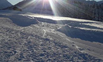 Eine sonnige Winterlandschaft mit schneebedecktem Boden. Die Sonne strahlt hinter den Bergen hervor und sorgt für eine helle, klare Atmosphäre. | © Panoramahütte