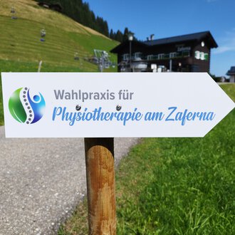 Ein Wegweiser zeigt zur Wahlpraxis für Physiotherapie am Zaferna. Die Umgebung ist grün und bergig, ideal für Erholung. | © Kleinwalsertal Tourismus | N. Lughammer