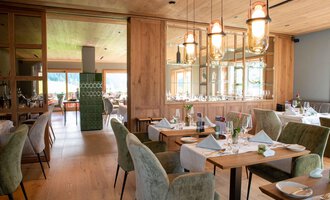 Ein modernes Restaurant mit Holzdekor und eleganten Tischen. Der Raum ist hell und einladend, mit gemütlichen Stühlen und stilvollen Leuchten. | © Almhof Rupp | Lukas Kind