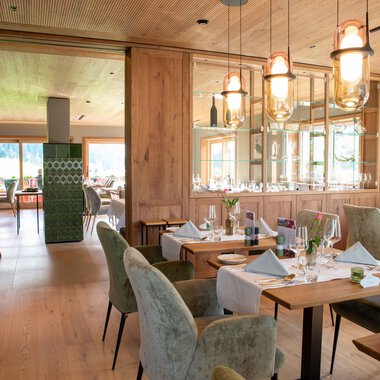 Ein modernes Restaurant mit Holzdekor und eleganten Tischen. Der Raum ist hell und einladend, mit gemütlichen Stühlen und stilvollen Leuchten. | © Almhof Rupp | Lukas Kind