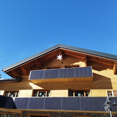 A modern wooden house with a balcony and photovoltaic panels. The clear blue sky creates a friendly atmosphere. | © Kleinwalsertal Tourismus | N. Lughammer