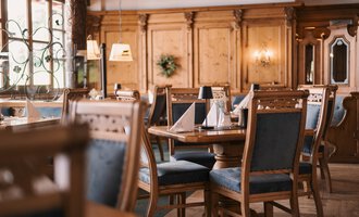 A cozy restaurant with wooden walls and elegant table decorations. The chairs are covered with blue fabrics and convey an inviting atmosphere.