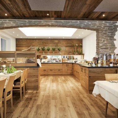 A cozy restaurant with wooden decor and an inviting buffet. The tables are elegantly set with green napkins. | © Robert Haller GmbH c/o Hotel Steinbock
