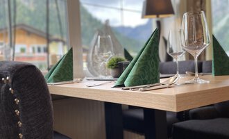 Ein eleganter Tisch mit grünen Servietten und Gläsern. Im Hintergrund sind Berge und Fenster, die viel Licht hereinlassen. | © Robert Haller GmbH c/o Hotel Steinbock
