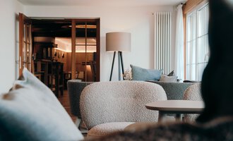 A modern living room with cozy sofas and a table. In the background, doors and a floor lamp can be seen.