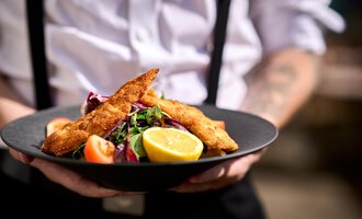 A plate with crispy fish fillets, served on a bed of fresh salad. Accompanied by lemon slices and a garnish of tomatoes. | © Hotel Tradizio | © Annette Sandner