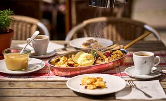 A rustic breakfast with Kaiserschmarrn, ice cream, and fresh fruits. Accompanied by a cup of coffee and a glass of pudding on a wooden table. | © Hotel Tradizio | © Annette Sandner