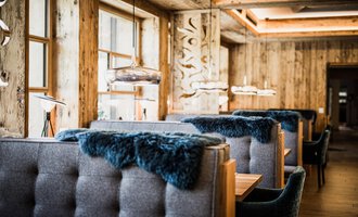 Ein modernes Restaurant mit gemütlichen Sitzbänken und warmem Holzdekor. Große Fenster sorgen für viel Licht und eine einladende Atmosphäre. | © Verwöhn- & Wellnesshotel Walserhof| Aileen Melucci