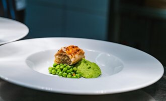 Ein hübsches Gericht auf einem weißen Teller, das gefüllte Teigtaschen mit einer Erbsenpüree und frischen Erbsen zeigt. Die Farben sind lebhaft und ansprechend. | © Verwöhn- & Wellnesshotel Walserhof| Frank Simon