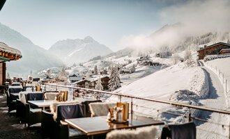 A beautiful view of a snowy mountain landscape with cozy tables on a terrace. The atmosphere is calm and inviting, surrounded by snow-covered hills and mountains.