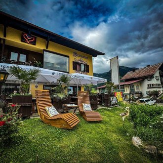Ein gemütliches Café mit einem einladenden Außenbereich. Zwei Liegestühle stehen auf einer grünen Wiese, umgeben von Pflanzen und Blick auf ein charmantes Gebäude. | © Ristorante Monte Zaferna | K. Harmat-Hegedüs