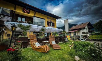 Ein gemütliches Café mit einem einladenden Außenbereich. Zwei Liegestühle stehen auf einer grünen Wiese, umgeben von Pflanzen und Blick auf ein charmantes Gebäude. | © Ristorante Monte Zaferna | K. Harmat-Hegedüs