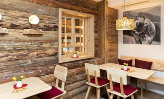 Ein gemütliches Café mit holzverkleideten Wänden und rustikalen Möbeln. An den Tischen stehen kleine Blumenvasen und es hängt ein Bild eines Tieres an der Wand. | © Schönegger Käse-Alm