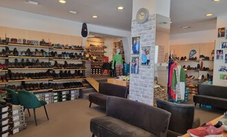 Ein Schuhgeschäft mit zahlreichen Regalen voller Schuhe. In der Mitte stehen bequeme Sofas und Kleidung ist zur Schau gestellt. | © Schuhhaus Schuster | Marietta Diehl