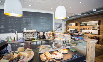 Ein modernes Café mit einer Auswahl an Backwaren und einer Verkaufstheke. Im Hintergrund sind Getränke und Lebensmittelregale sichtbar. | © Kleinwalsertal Tourismus | Frank Drechsel