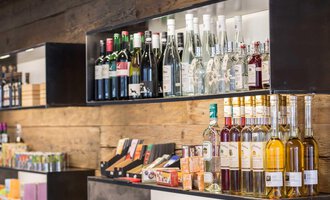 Regale mit verschiedenen alkoholischen Getränken und Snacks. Die Regale sind aus Holz und zeigen eine Auswahl an Weinen und Spirituosen. | © Kleinwalsertal Tourismus | Frank Drechsel