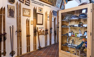 An exhibition featuring several wooden skis displayed on walls. In the background, photos and information about ski history are visible. | © Kleinwalsertal Tourismus | Oliver Farys