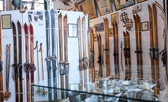 An exhibition with various old skis on the walls. In the foreground, there are glass cases with further collectibles on display. | © Kleinwalsertal Tourismus | Oliver Farys