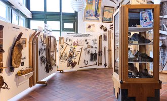 An exhibition room with historical tools and weapons on the walls. In a display case, further objects are showcased. | © Kleinwalsertal Tourismus | Oliver Farys
