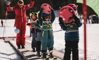 A ski school for children in the snow. The children are wearing helmets and holding ski boards as they get ready for the slopes.