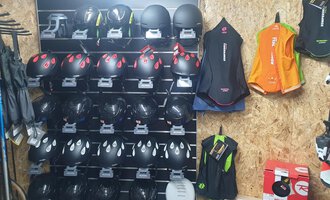 A wall with several helmets and suits for sports activities. The helmets are black with red accents, while the suits are in various colors. | © IFA Hotel Alpenrose