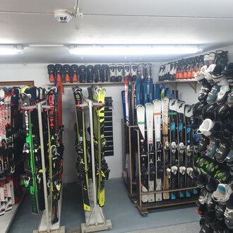 A room with several skis and ski boots, neatly stacked on shelves. The lighting is bright and it looks like a ski rental. | © IFA Hotel Alpenrose