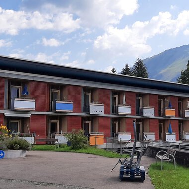 Ein modernes Gebäude mit mehreren Etagen und Balkonen. Die Umgebung ist grün mit Blick auf die Berge. | © Kleinwalsertal Tourismus | Veronika Senn