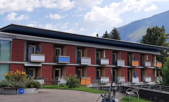 Ein modernes Gebäude mit mehreren Etagen und Balkonen. Die Umgebung ist grün mit Blick auf die Berge. | © Kleinwalsertal Tourismus | Veronika Senn