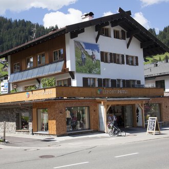 Ein charmantes Gebäude mit traditioneller Architektur, umgeben von Bergen. Im Erdgeschoss befindet sich ein Geschäft mit großen Fenstern. | © Sport Pauli Matthias Bischof e.U