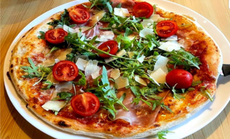 Eine köstliche Pizza mit Schinken, Kirschtomaten und frischem Rucola. Der Käse und die Kräuter verleihen ihr ein ansprechendes Aussehen.