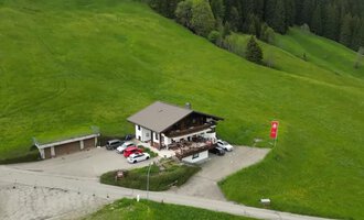 Ein gemütliches Gebäude in der Natur mit grünen Wiesen. Mehrere Autos parken vor dem Haus, das von Bäumen umgeben ist.