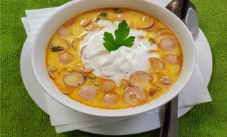 Eine leckere Suppe mit Wurstscheiben und einer cremigen Sahnehaube. Frische Kräuter garnieren das Gericht.
