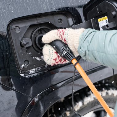 Eine Person lädt ein Elektroauto bei kaltem Wetter auf. Die Hand ist mit einer warmen, gestrickten Handschuh umgeben. | © Kleinwalsertal Tourismus | Oliver Farys