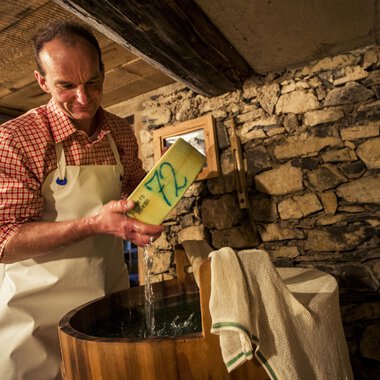 Ein Mann steht an einem Holztrog und gießt etwas hinein. Im Hintergrund sind steinerne Wände zu sehen. | © Kleinwalsertal Tourismus | Oliver Farys