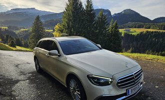 Ein elegantes Auto steht auf einer malerischen Straße in den Bergen. Im Hintergrund sind grüne Wiesen und bewaldete Hügel zu sehen. | © Taxi Beranek | Elmar Beranek
