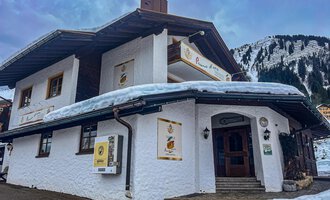 A charming building in Alpine style, surrounded by snow and mountains. The facade is white and invites you to linger. | © Trattoria Pomo d'oro | K. Harmat-Hegedüs