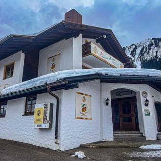 Ein charmantes Gebäude im alpinen Stil, umgeben von Schnee und Bergen. Die Fassade ist weiß und lädt zum Verweilen ein. | © Trattoria Pomo d'oro | K. Harmat-Hegedüs