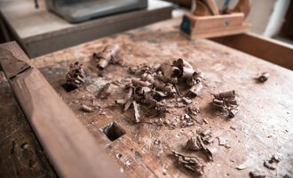 Eine Holzwerkbank mit Spänen und Holzresten. Im Hintergrund sind Werkzeuge zu sehen. | © Türtscher Die Schreinermanufaktur